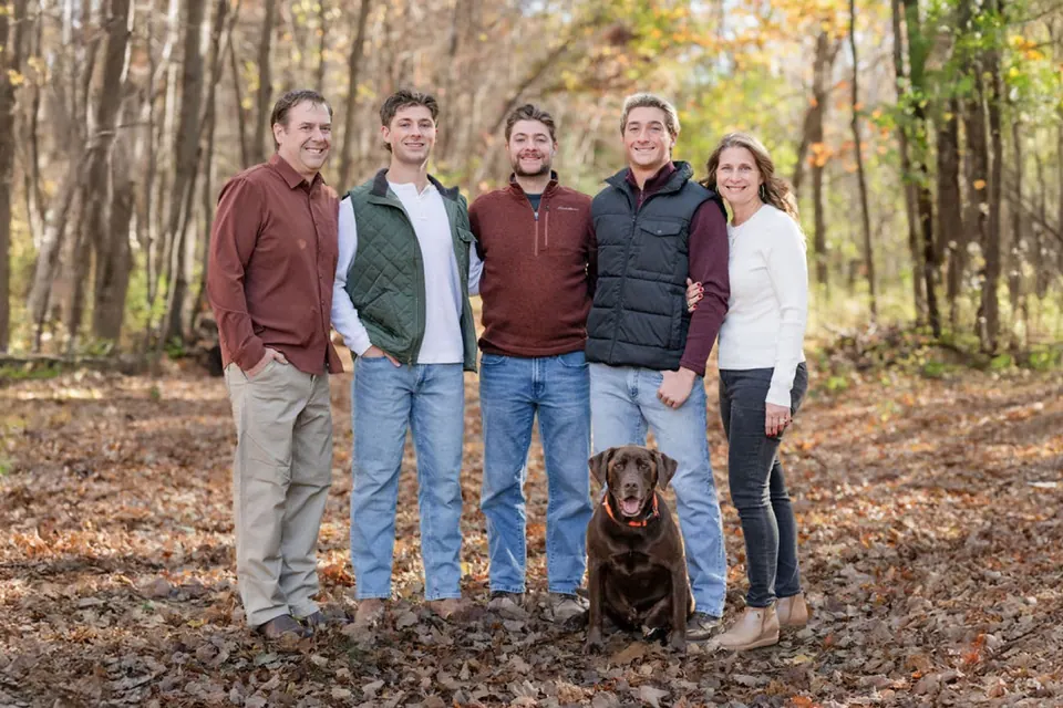 The Bowe family and their chocolate Lab in the autumn woods